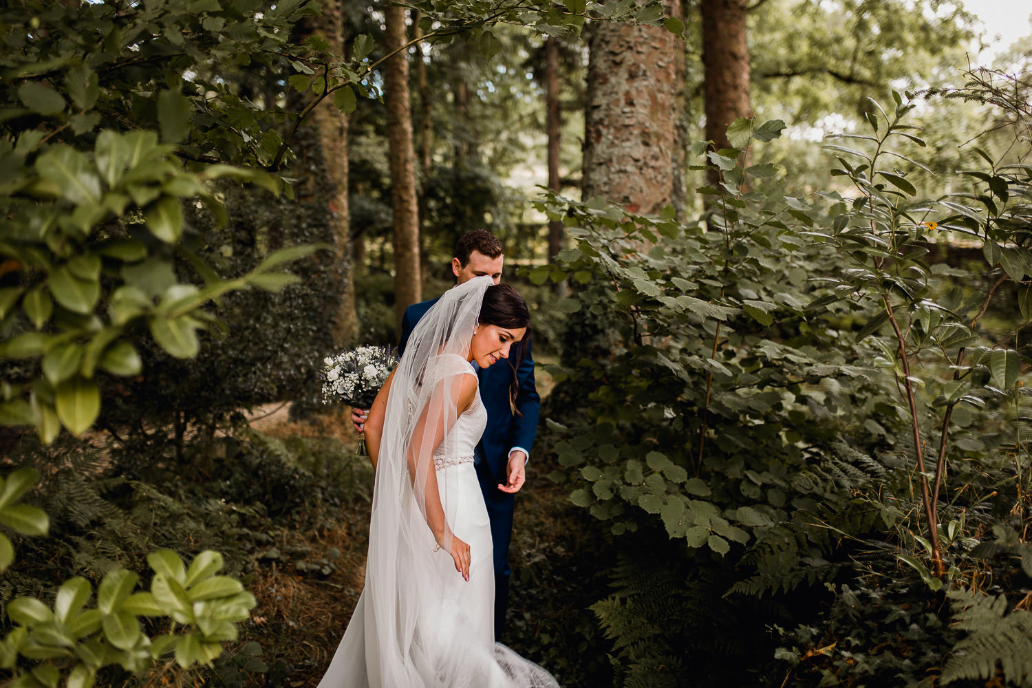 bride and groom walking through a forest