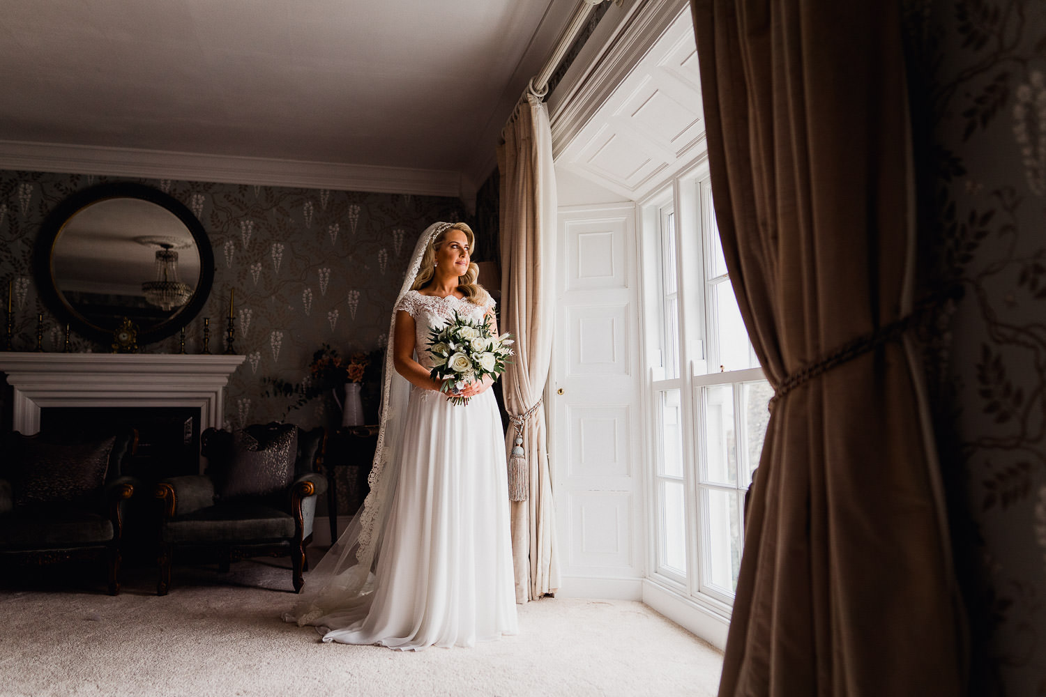 bride standing in window light holding flowers