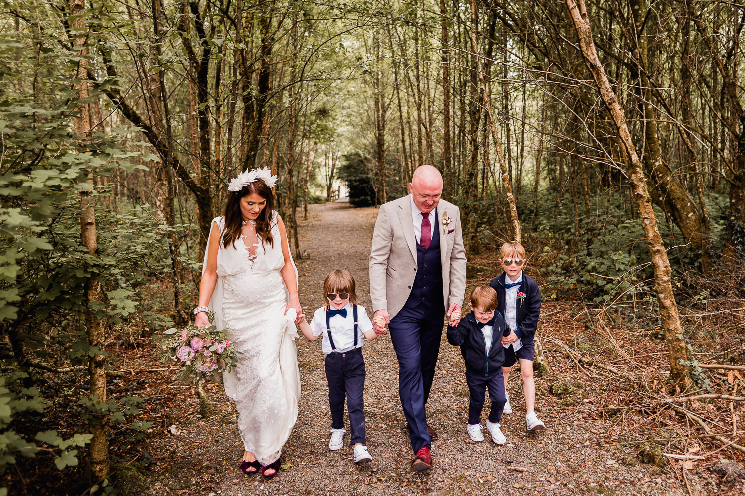 bride and groom walking through a forest with their kids
